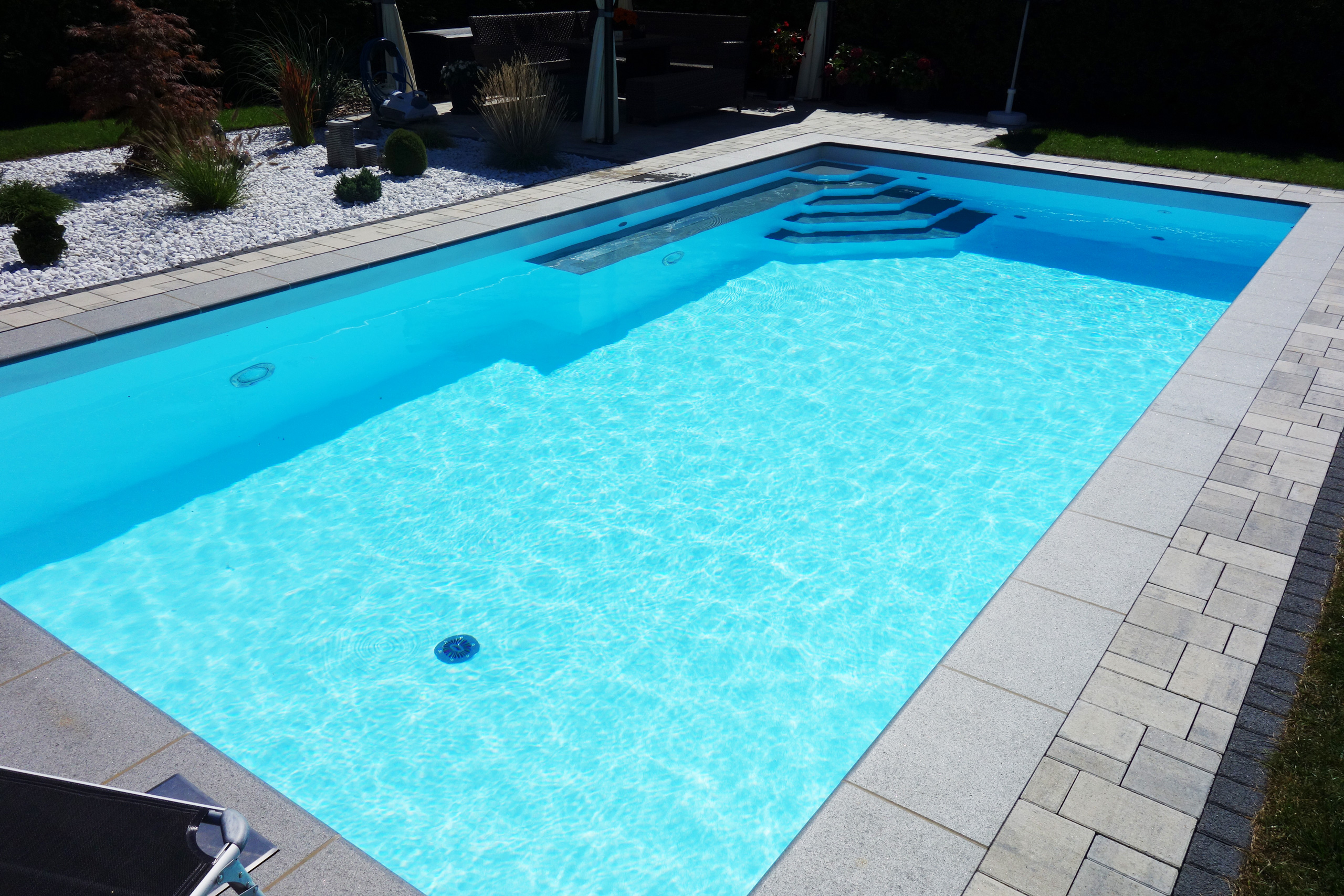 Rechteckbecken 4x8x1,5m mit Ecktreppe, Podest und Luftsprudelsitz im Garten, umgeben von Pflastersteinen.