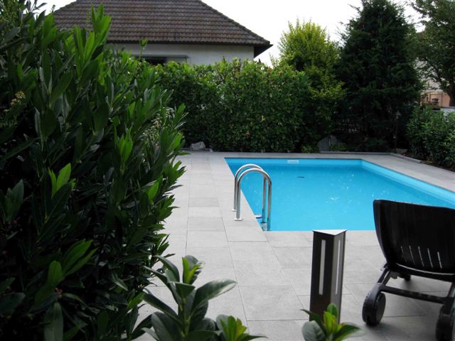 Türkises Schwimmbecken 3,5x7x1,5m mit Einstiegsleiter und umlaufender Poolumrandung im Garten.