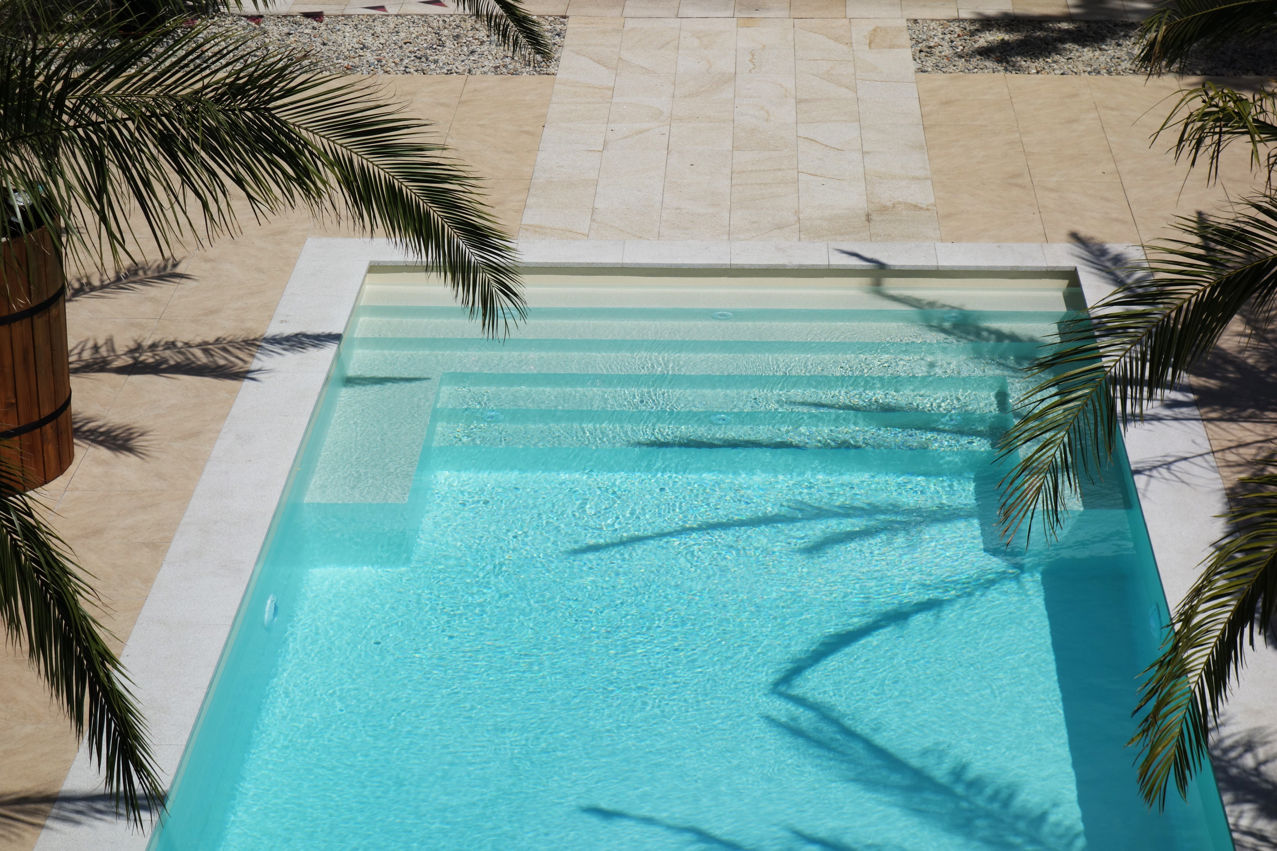 Blick von oben auf das Schwimmbad mit gerader Treppe, Podest und türkisblauem Wasser