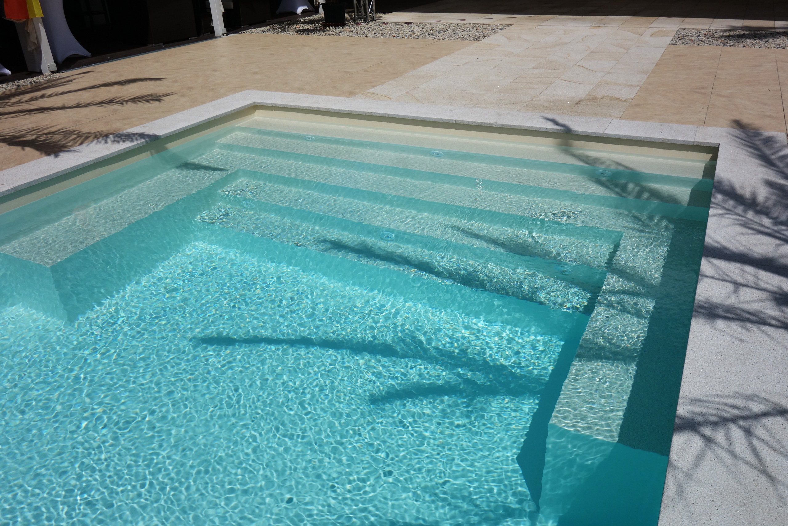 Blick auf die gerade Treppe und das Podest eines Schwimmbads mit hellblauer Einhängefolie und Wasserspiegelungen.