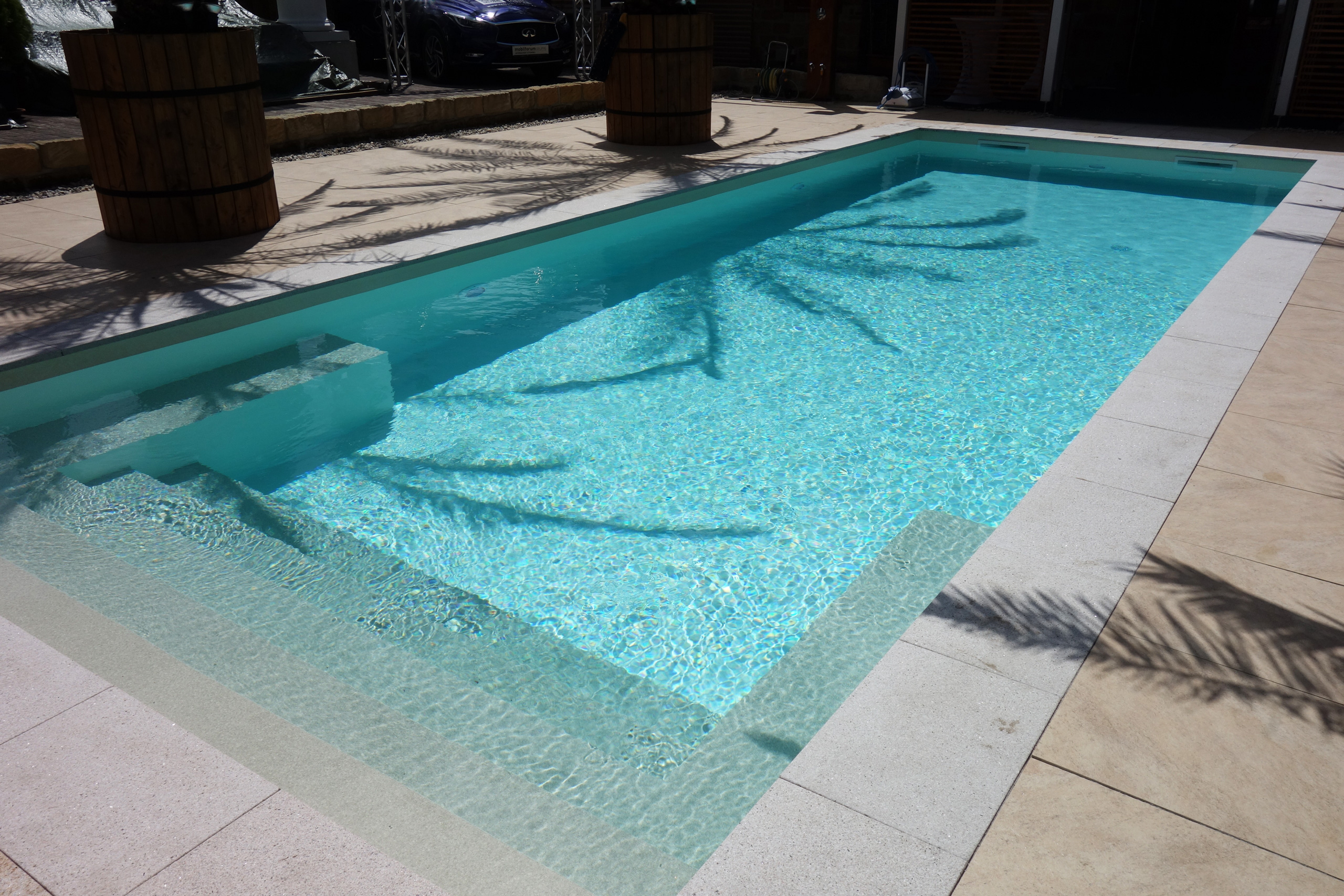 Gerade Treppe und Podest im Schwimmbad, umgeben von hellen Poolrandplatten und beigen Terrassenfliesen.