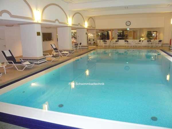 Helles Hallenbad mit Überlaufrinne, blauer Poolfolie und Liegen am Beckenrand