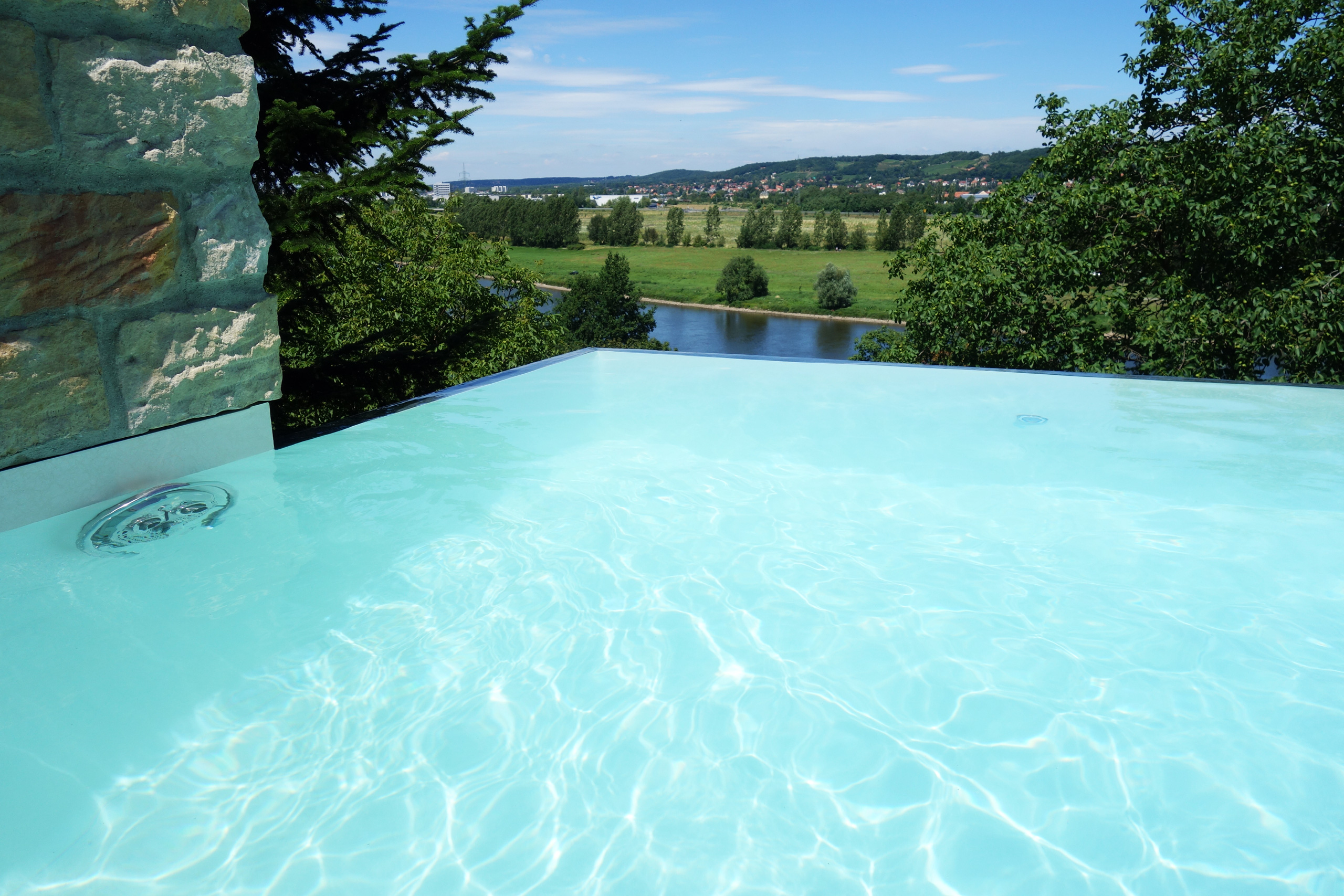 Überlaufbecken Infinity Pool mit Wassereinlauf und Blick auf Flusslandschaft