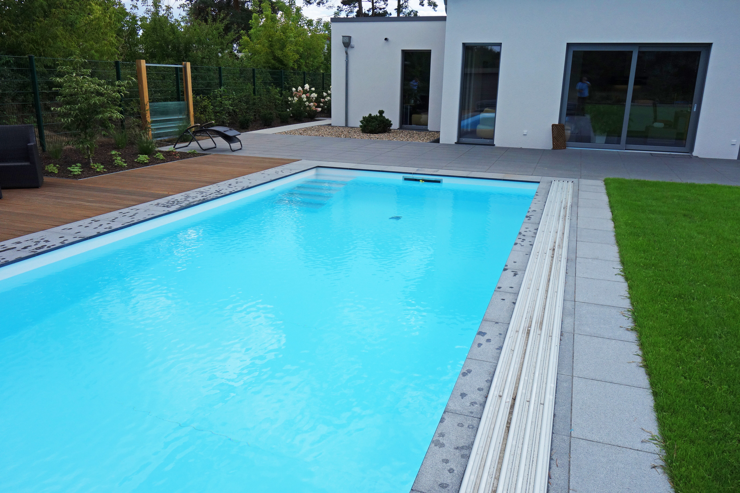 Außenpool mit blauer Folie, grauen Fliesen, Holzterrasse und teilweiser Poolabdeckung