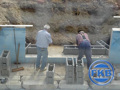 Zwei Arbeiter beim Bau einer Beckentreppe aus Betonsteinen für eine Beckensanierung in Hellblau