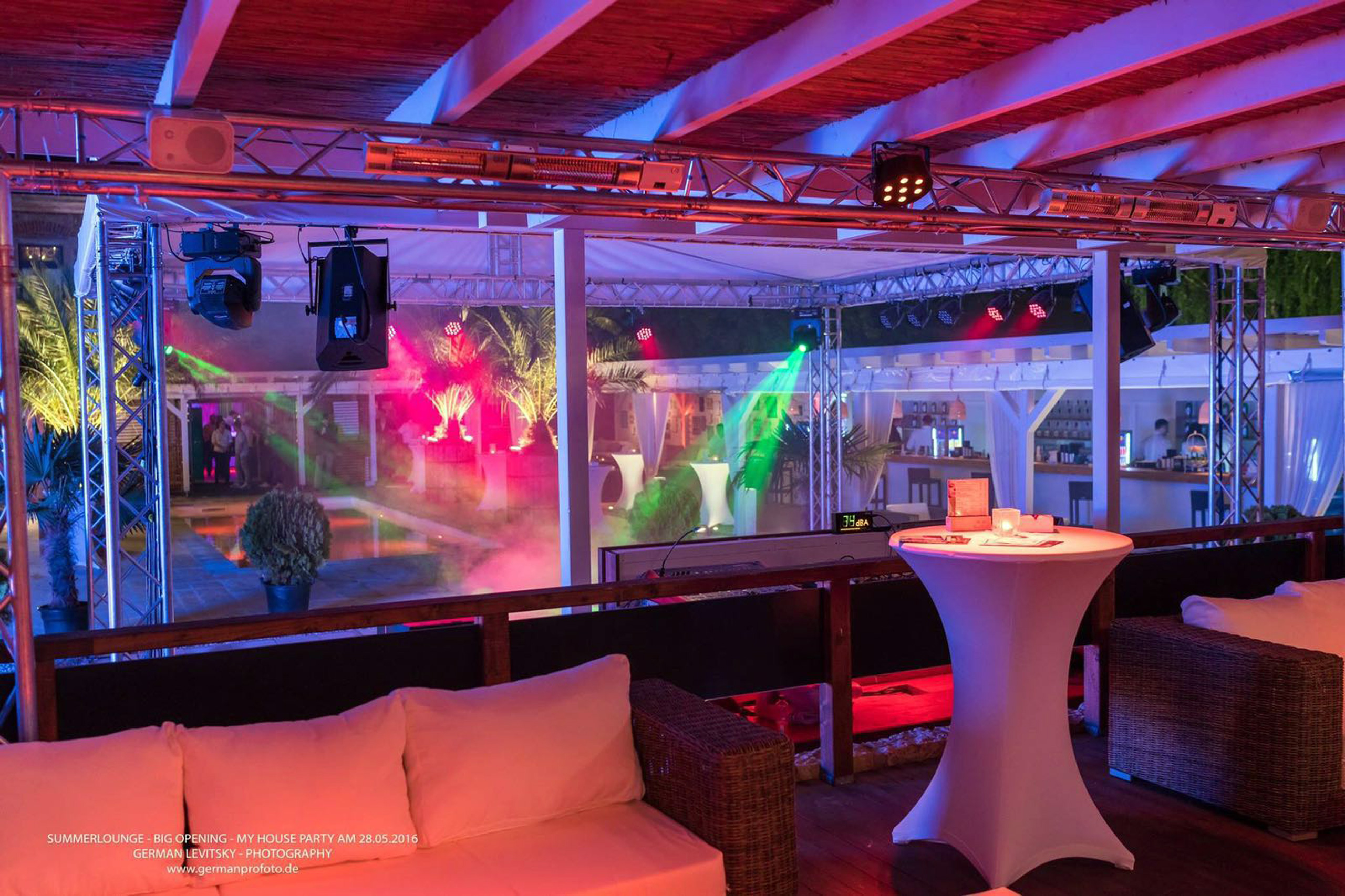 Party-Beleuchtung und Lounge-Möbel auf einer Terrasse mit Blick auf ein Schwimmbad bei Nacht