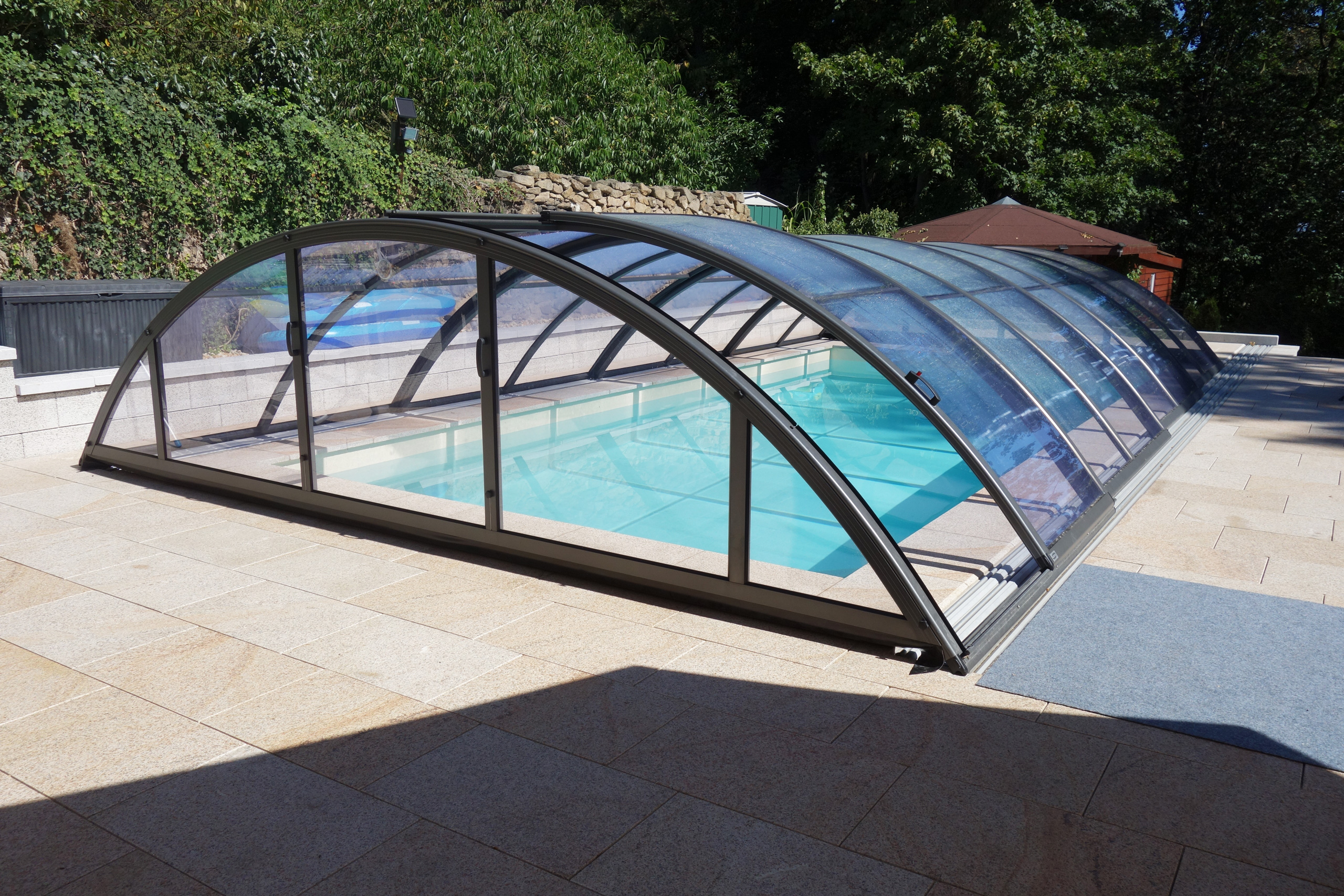 Poolüberdachung Klasik Clear über einem Rechteckpool mit Ecktreppe, Podest und Stehstufe