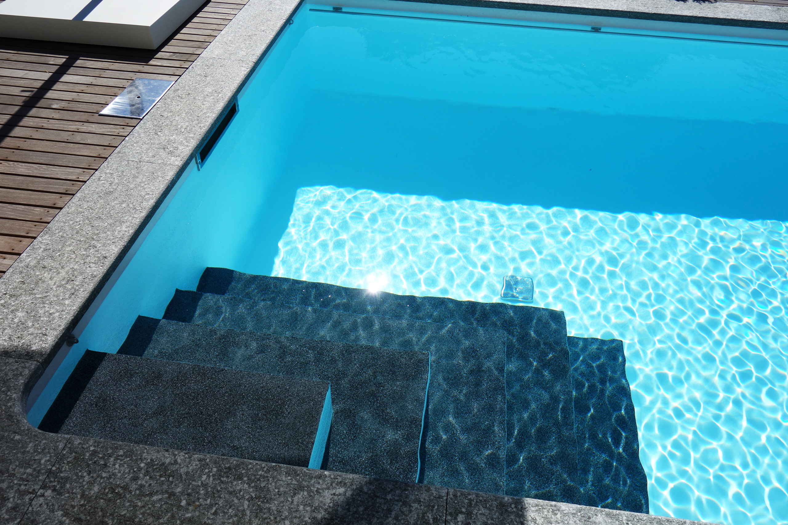 Detailansicht der Ecktreppe eines Rechteckbeckens mit Unterflurabdeckung und blauer Poolfolie.