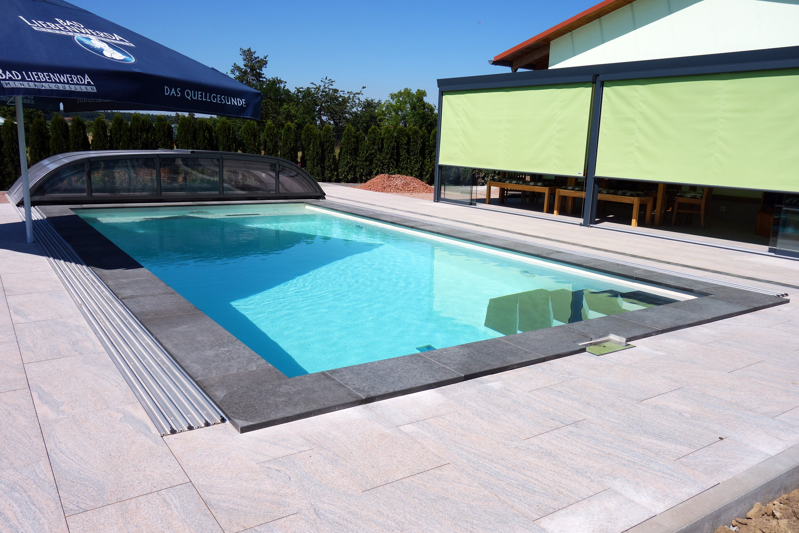 Rechteck-Schwimmbad mit blauer Wasseroberfläche, Rollladenabdeckung und dunklem Beckenrand.