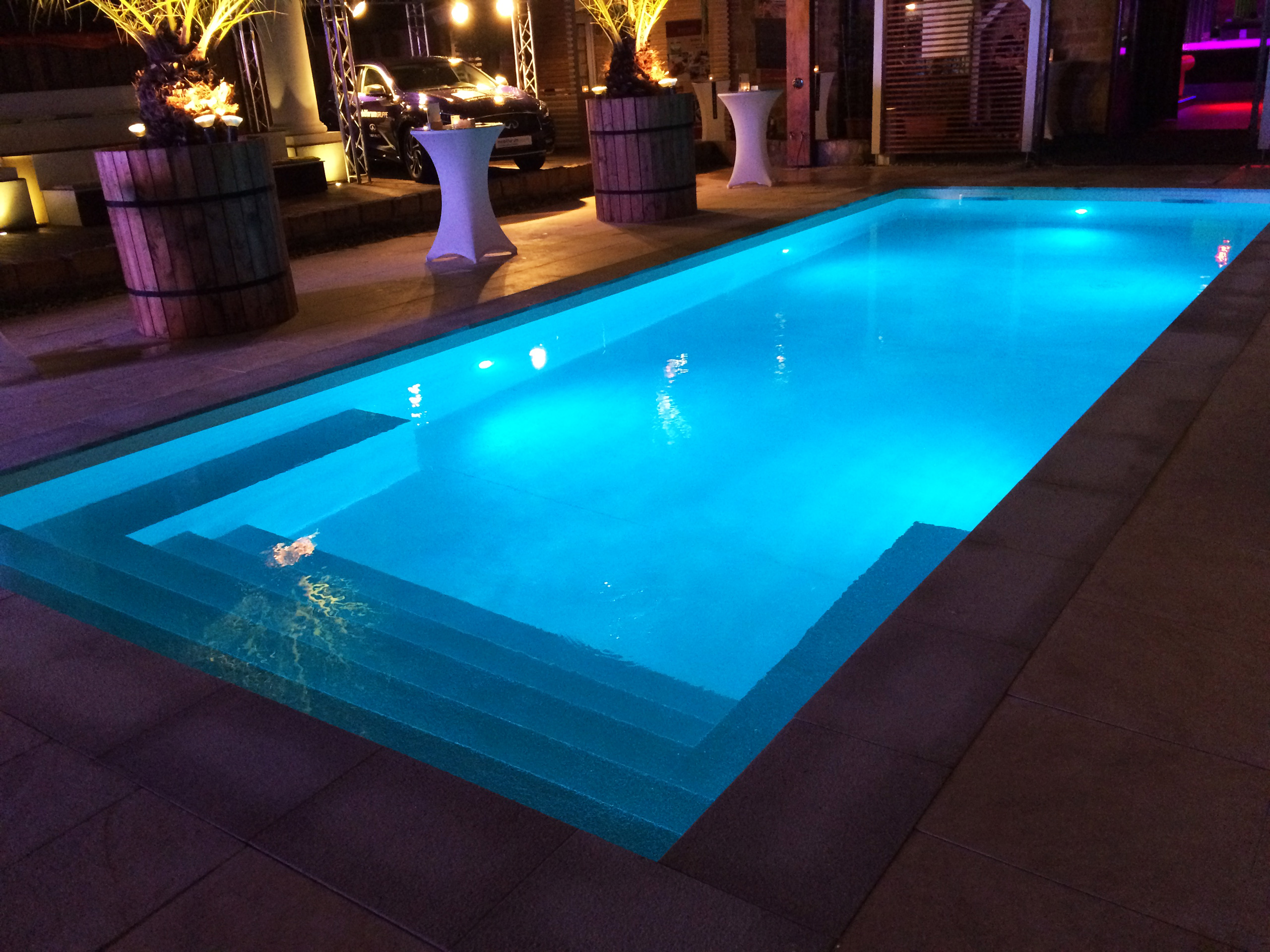 Beleuchtetes Schwimmbad 4x10x1,35m mit gerader Treppe und Podest bei Nacht, umgeben von Dekoration.