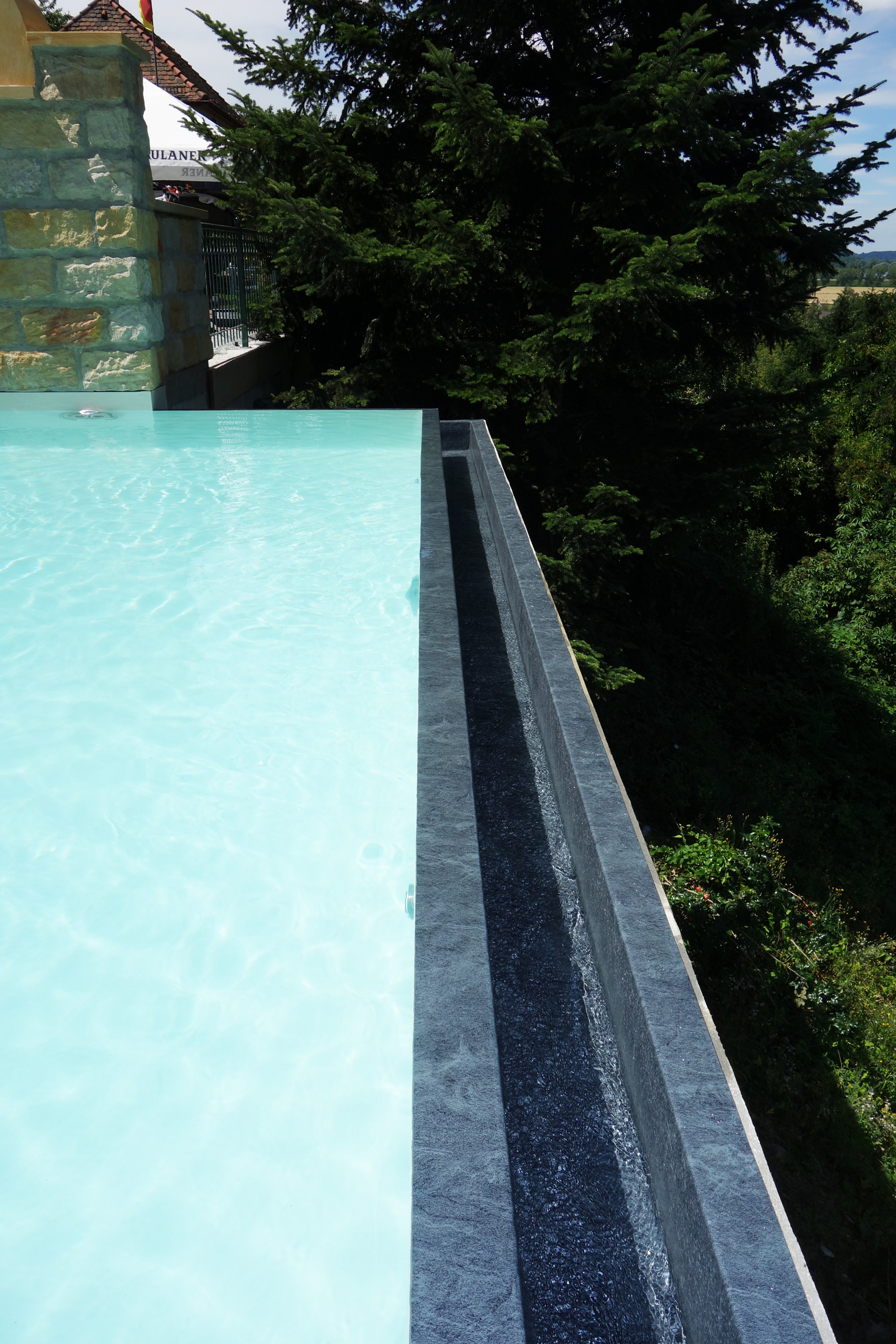 Detailansicht des Überlaufkanals eines Infinity Pools mit fließendem Wasser und angrenzender Natur
