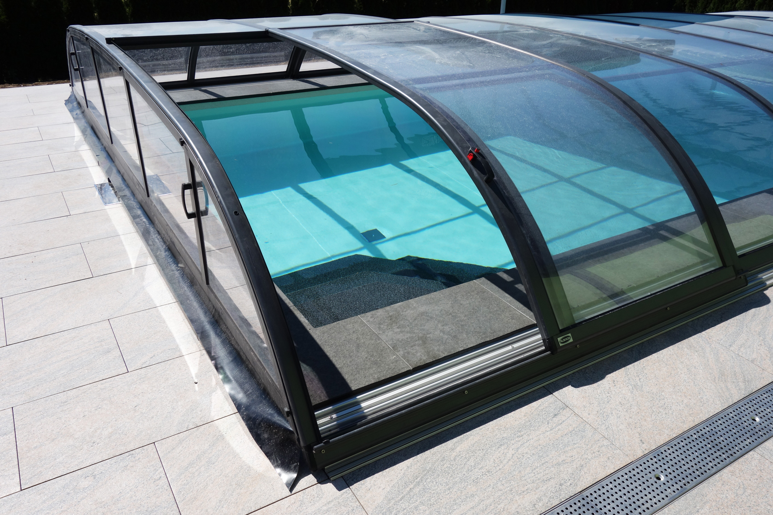 Detailansicht der Poolüberdachung mit Schiebeelementen und hellen Fliesen am Beckenrand.