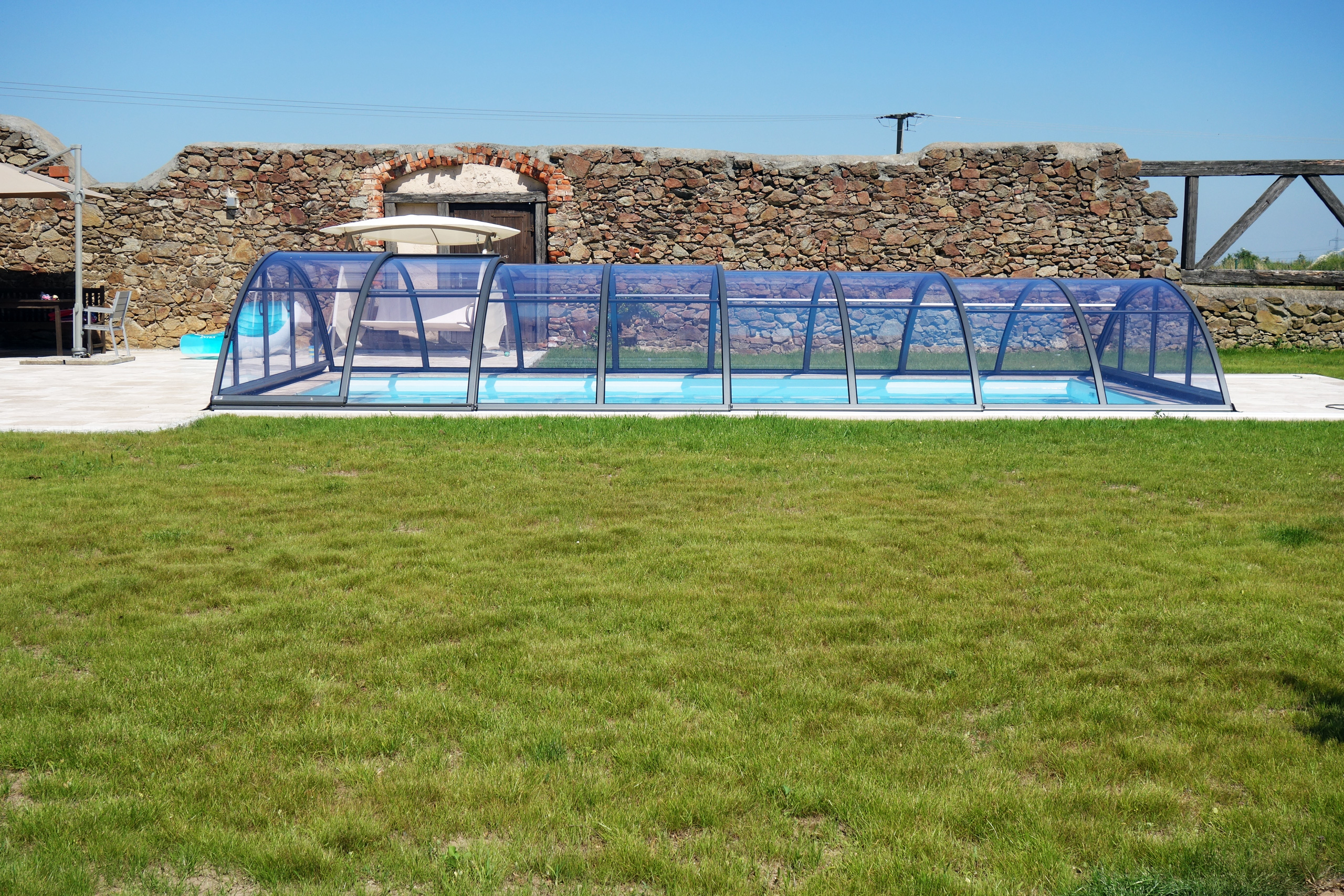 Schwimmbecken mit blauer Abdeckung und Steinmauer im Hintergrund, umgeben von Rasen