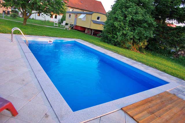 Rechteckbecken mit blauer Einhängefolie, umrandet von hellgrauen Fliesen und einer Holzterrasse