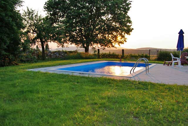 Rechteckbecken mit blauer Einhängefolie im Garten bei Sonnenuntergang, mit Einstiegsleiter und Liegestühlen