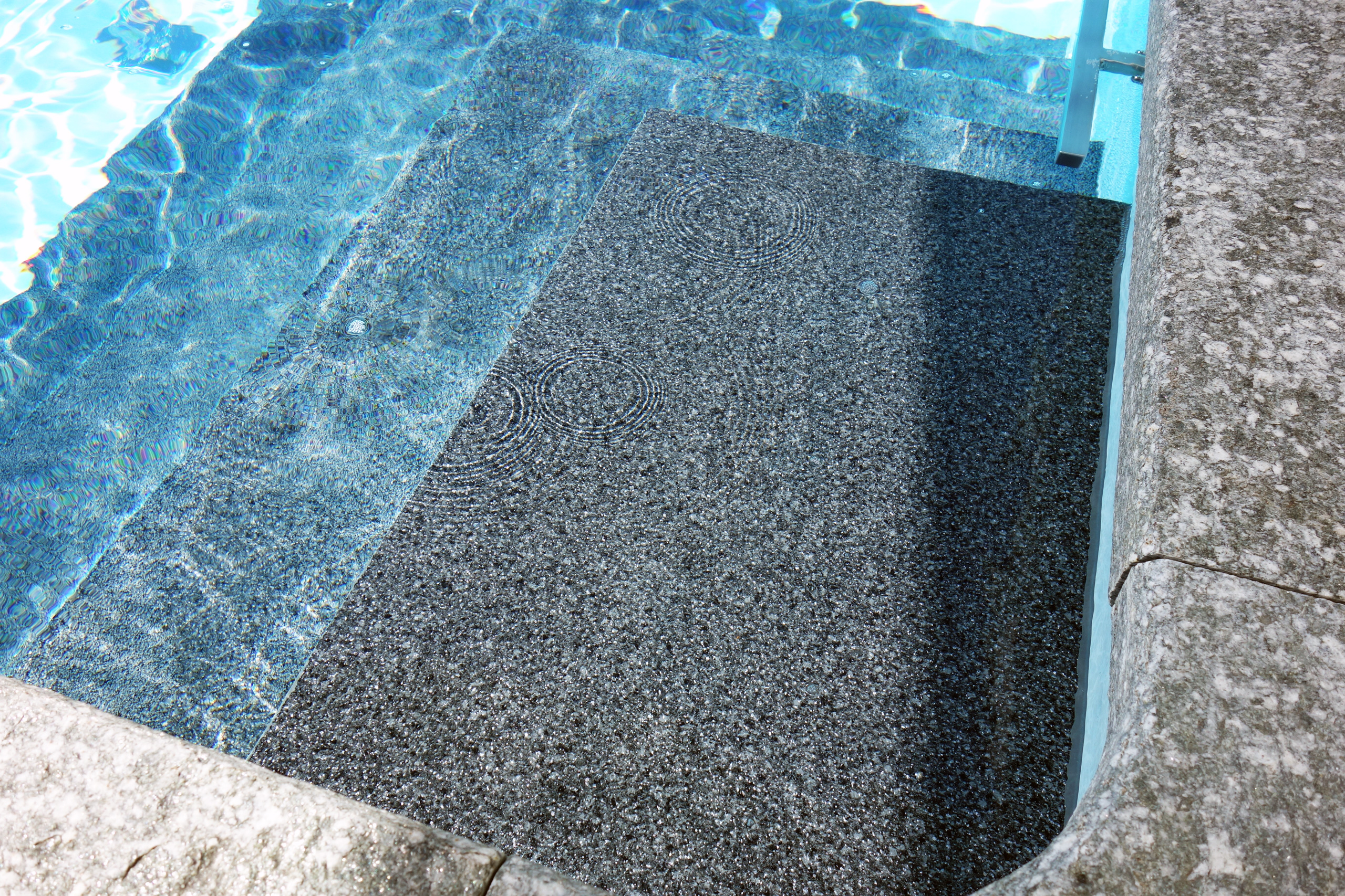 Detailansicht der grauen Ecktreppe mit Podest im Rechteckbecken, umgeben von blauem Poolwasser.