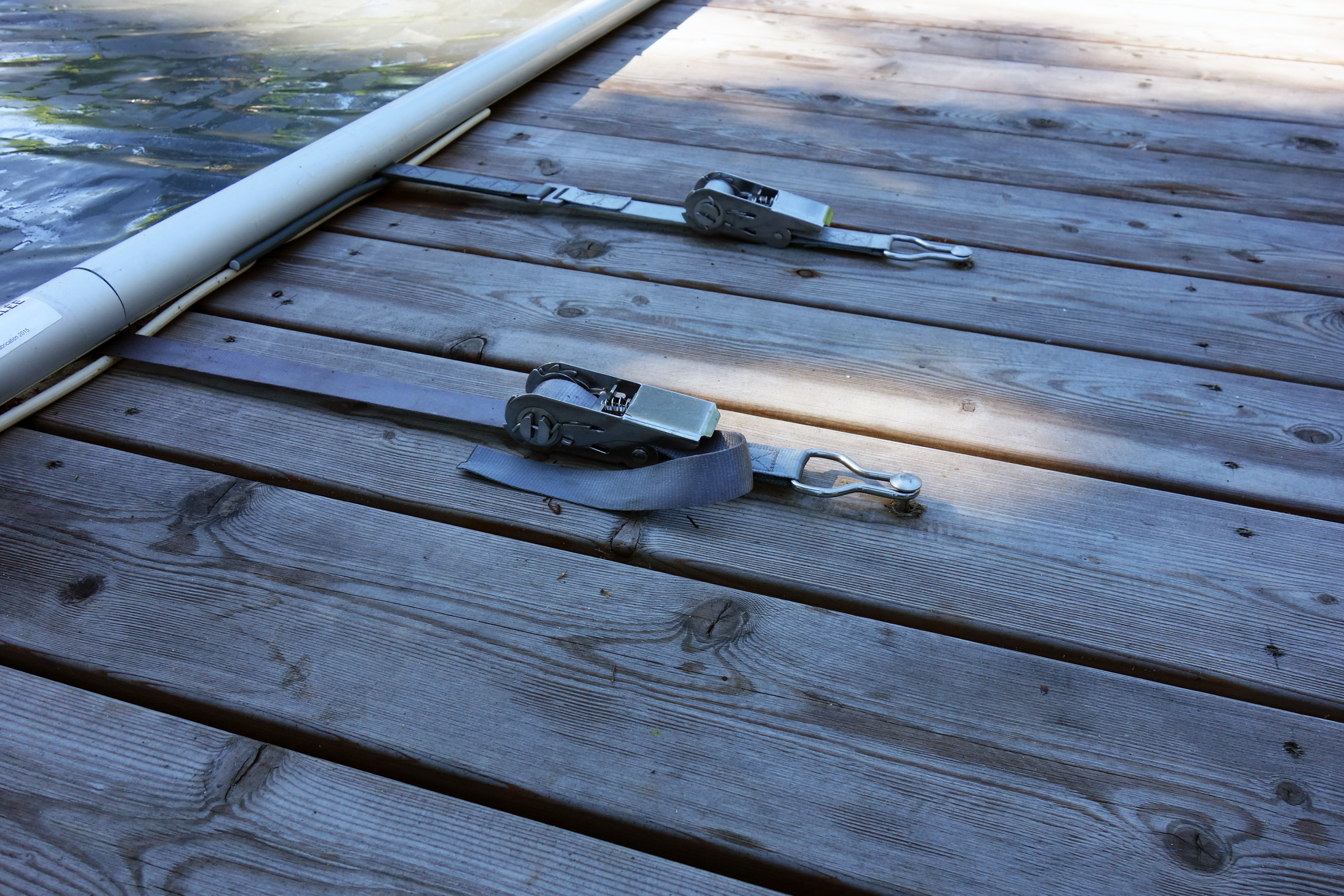 Spanngurte auf Holzsteg befestigen die weiße Poolabdeckung, Wasseroberfläche im Hintergrund