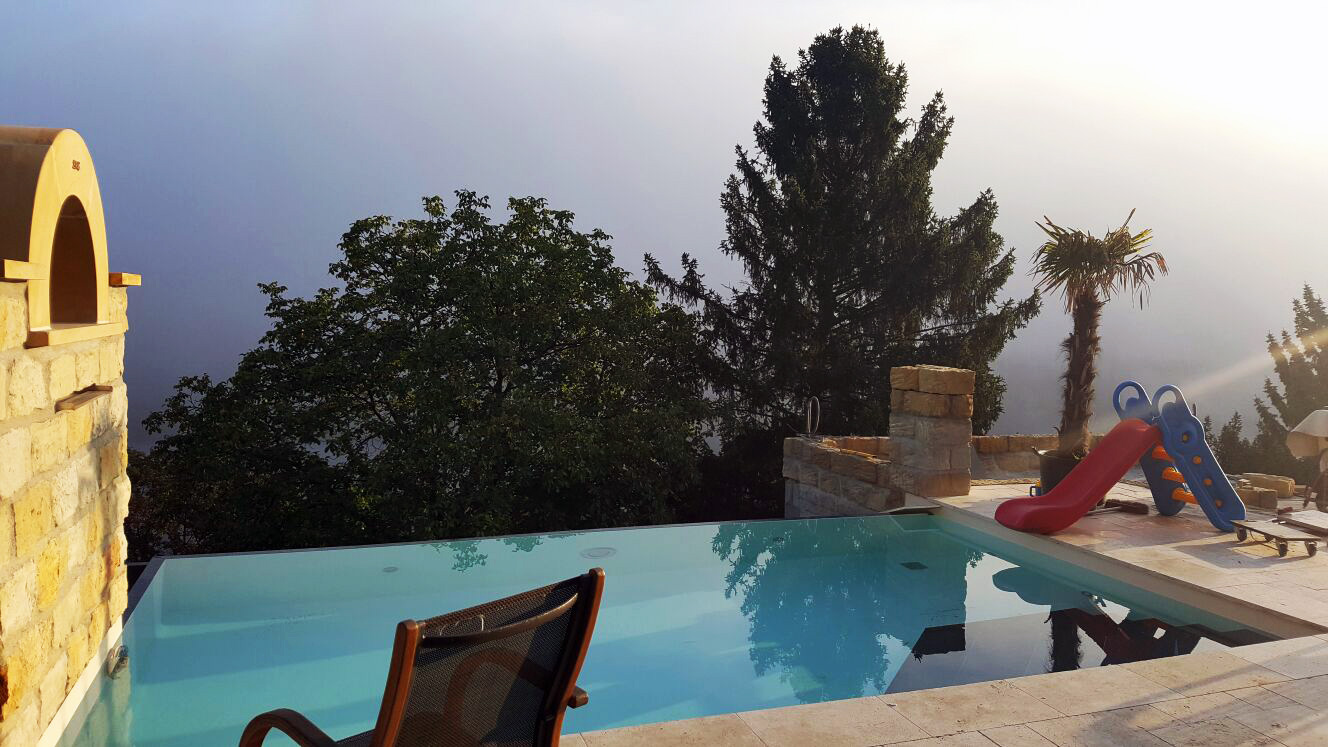 Infinity Pool mit blauer Wasseroberfläche, umgeben von Bäumen und einem Kinderbecken mit Rutsche