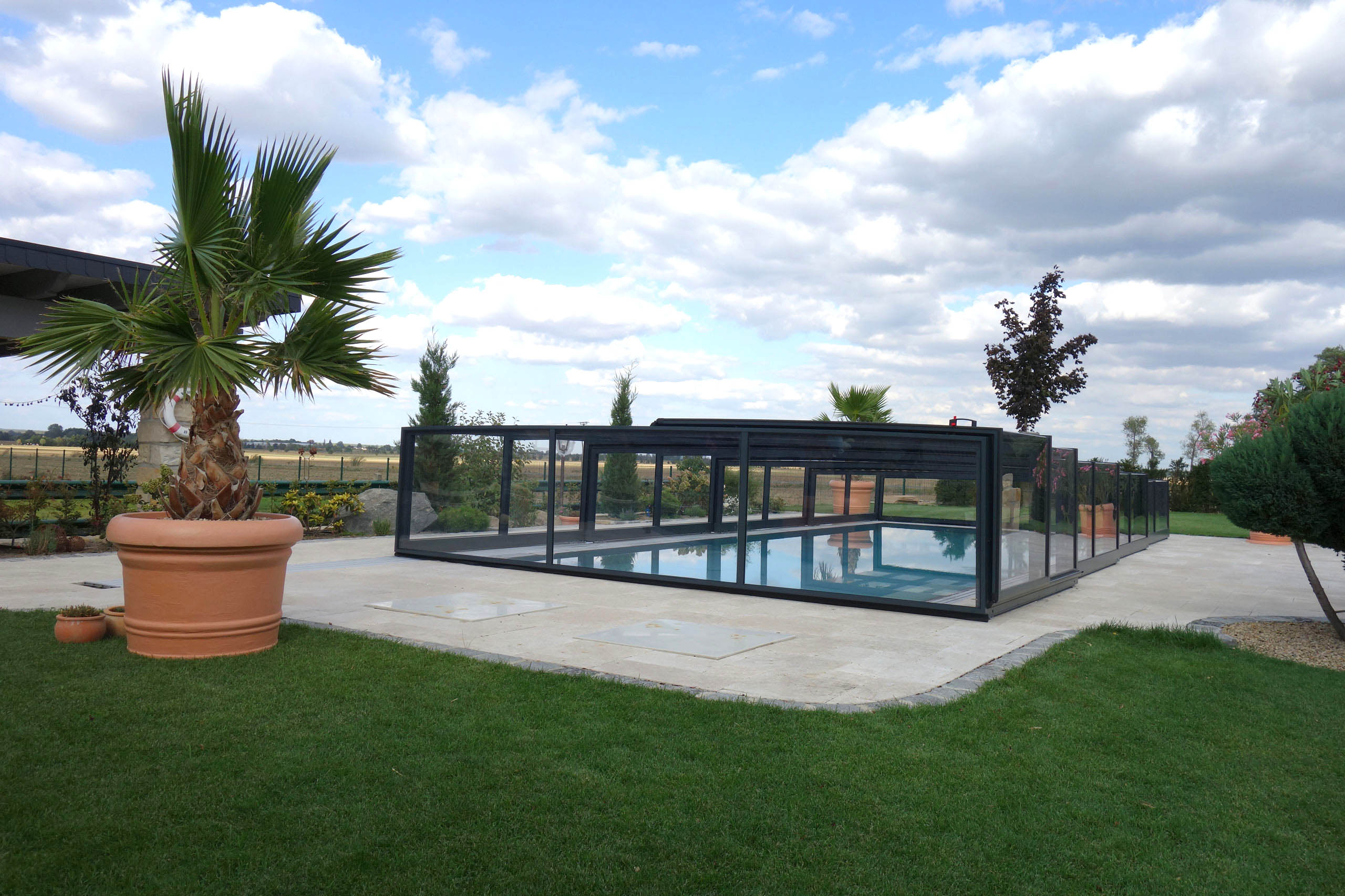 Poolüberdachung Prestige Plus mit transparenten Seitenwänden und schwarzem Rahmen im Garten.