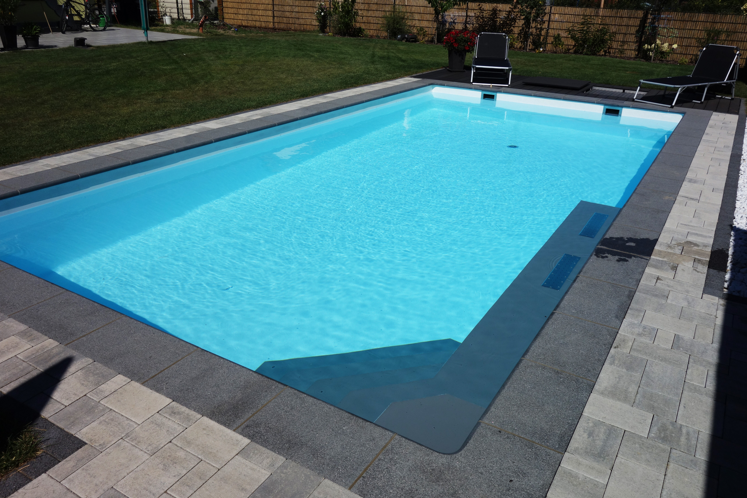 Rechteckbecken mit Ecktreppe, Podest und Luftsprudelsitz von oben, umgeben von Pflastersteinen und Rasen