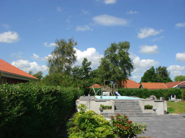 Blick auf ein Becken mit GSA und Schwalldusche, umgeben von Hecken und Häusern unter blauem Himmel.