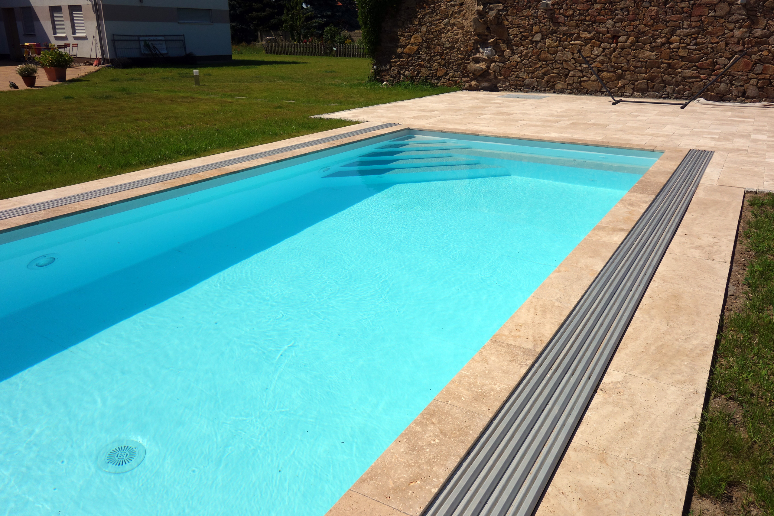 Beckenrand mit beige-braunen Fliesen, daneben eine graue Poolabdeckung