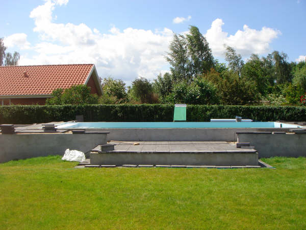 Gartenansicht eines Pools mit Schwalldusche, umgeben von einer Hecke und einem Haus im Hintergrund