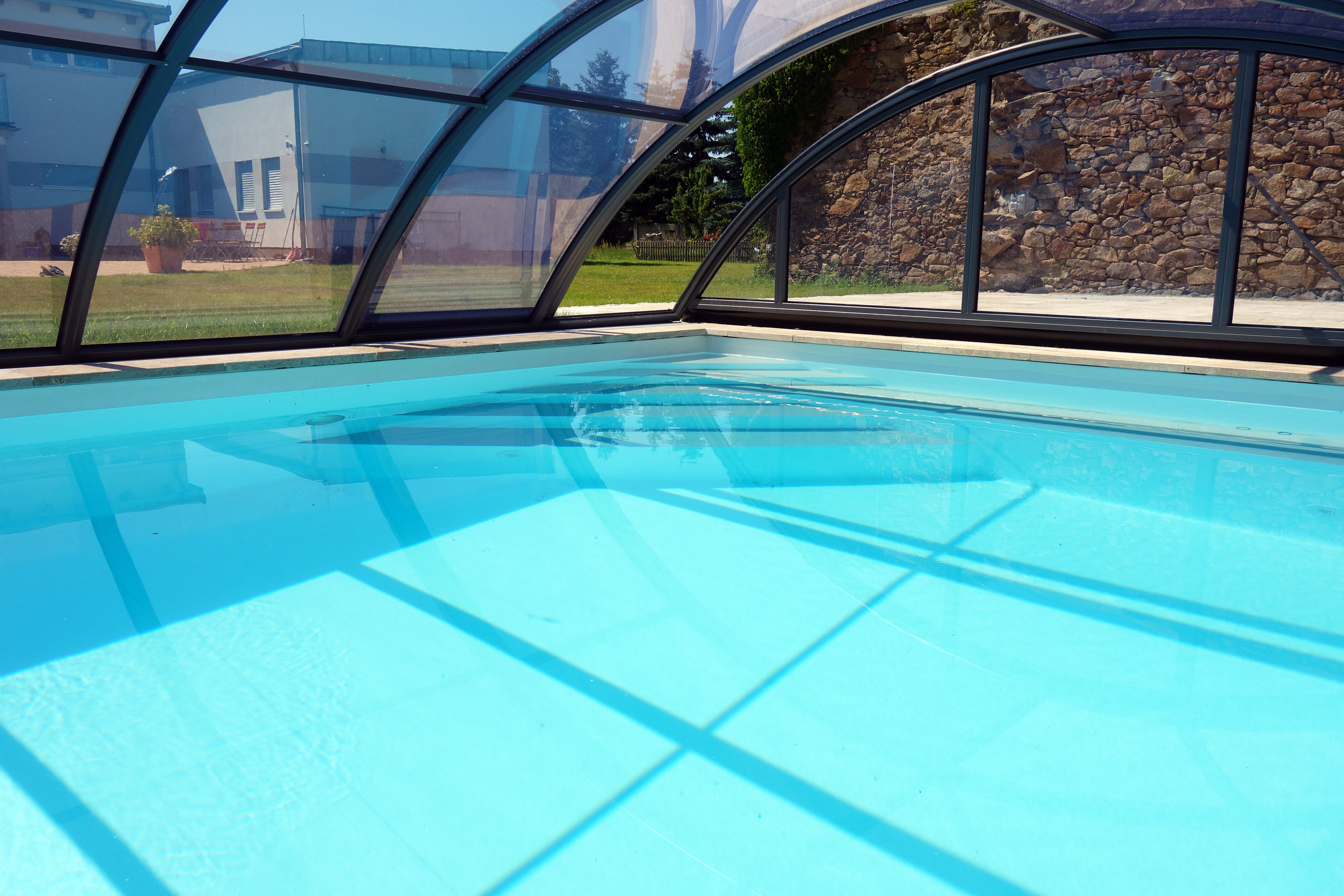 Schwimmbecken mit blauer Folie unter einer transparenten Poolüberdachung