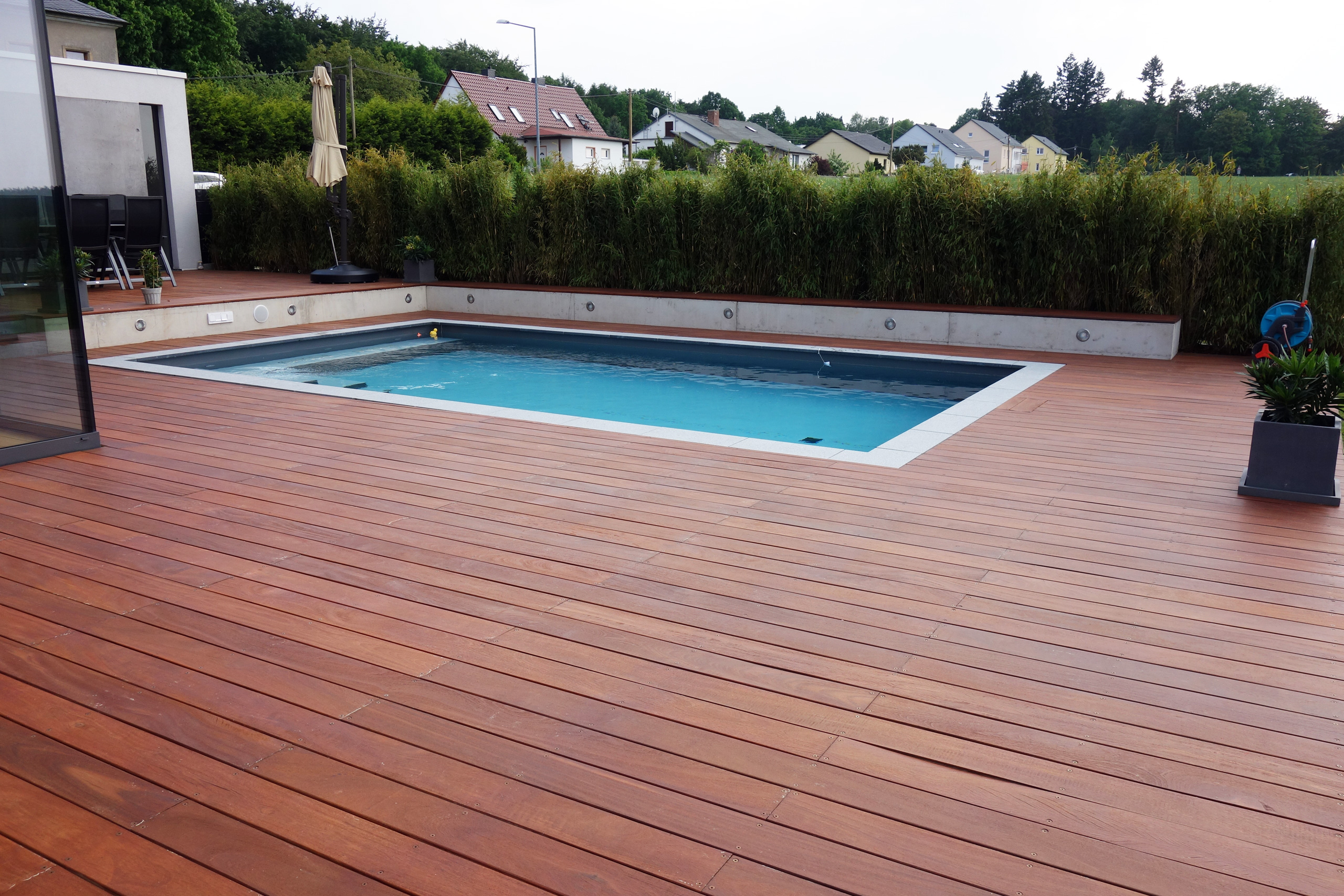 Betonbecken 3,5x7x1,5m mit Ecktreppe und Podest, umgeben von Holzterrasse und Bambushecke