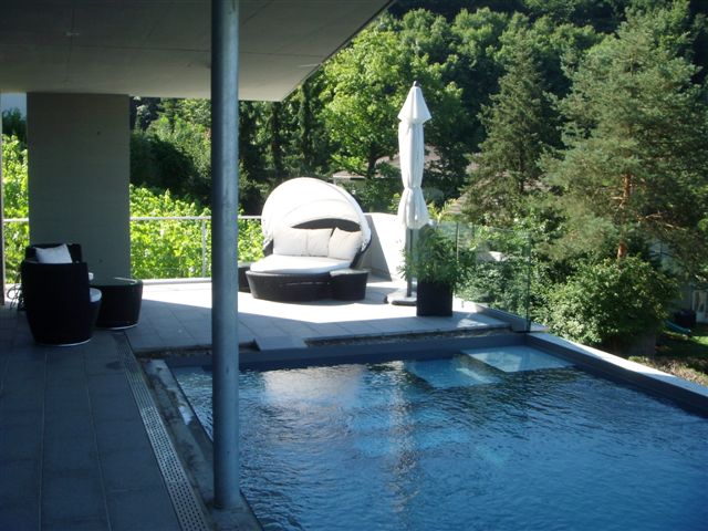 Modernes Schwimmbecken mit Granit-Optik, integrierter Treppe und angrenzender Terrasse mit Lounge-Möbeln.