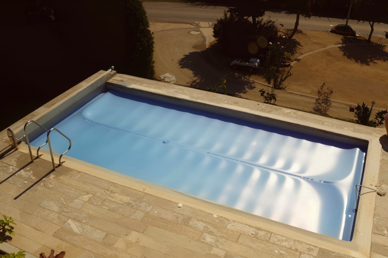 Blaue Isolierabdeckung BAC-Poolsystems Isola vollständig auf einem rechteckigen Pool ausgebreitet, mit Poolleiter.