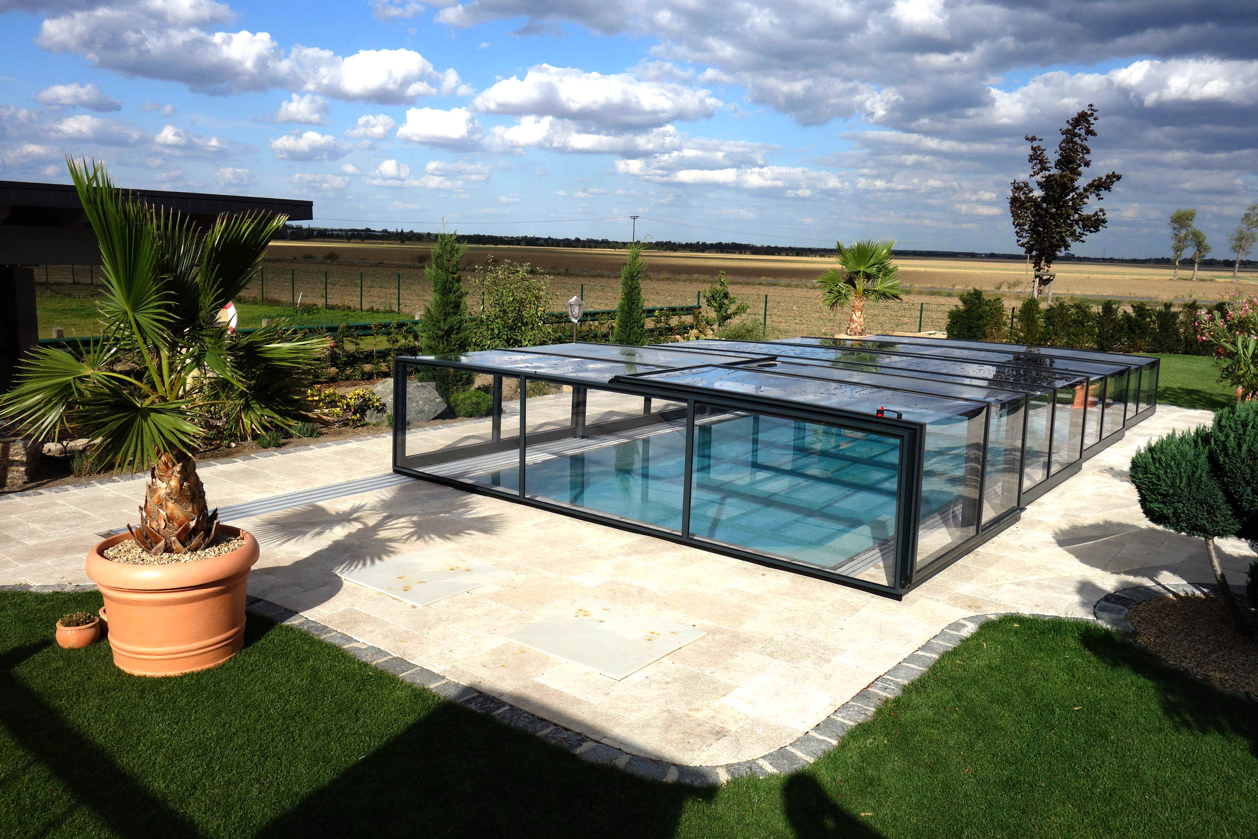 Poolüberdachung Prestige Plus mit transparenten Seitenwänden und Dach in einer Gartenanlage