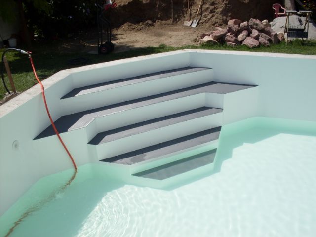 Trapezförmige Treppe eines L-Form Schwimmbeckens, mit grauen Stufen und weißer Folie, teilweise gefüllt