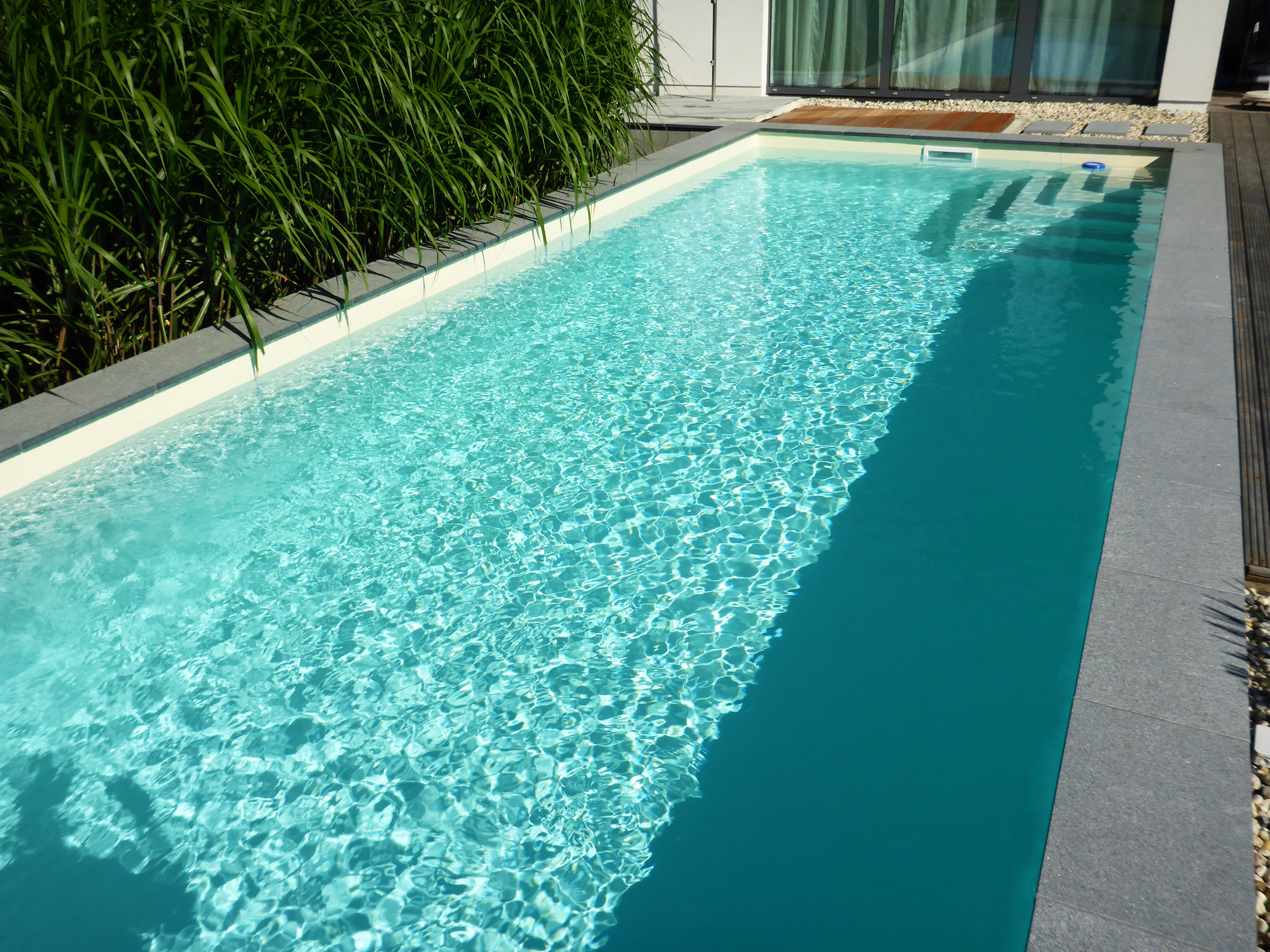 Detailansicht des herausstehenden Swimmingpools mit Ecktreppe und türkisblauem Wasser.
