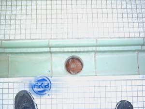 Alte Fliesen und ein offenes Rohr im Beckenboden eines Hallenbades vor der Sanierung mit weißer Folie.