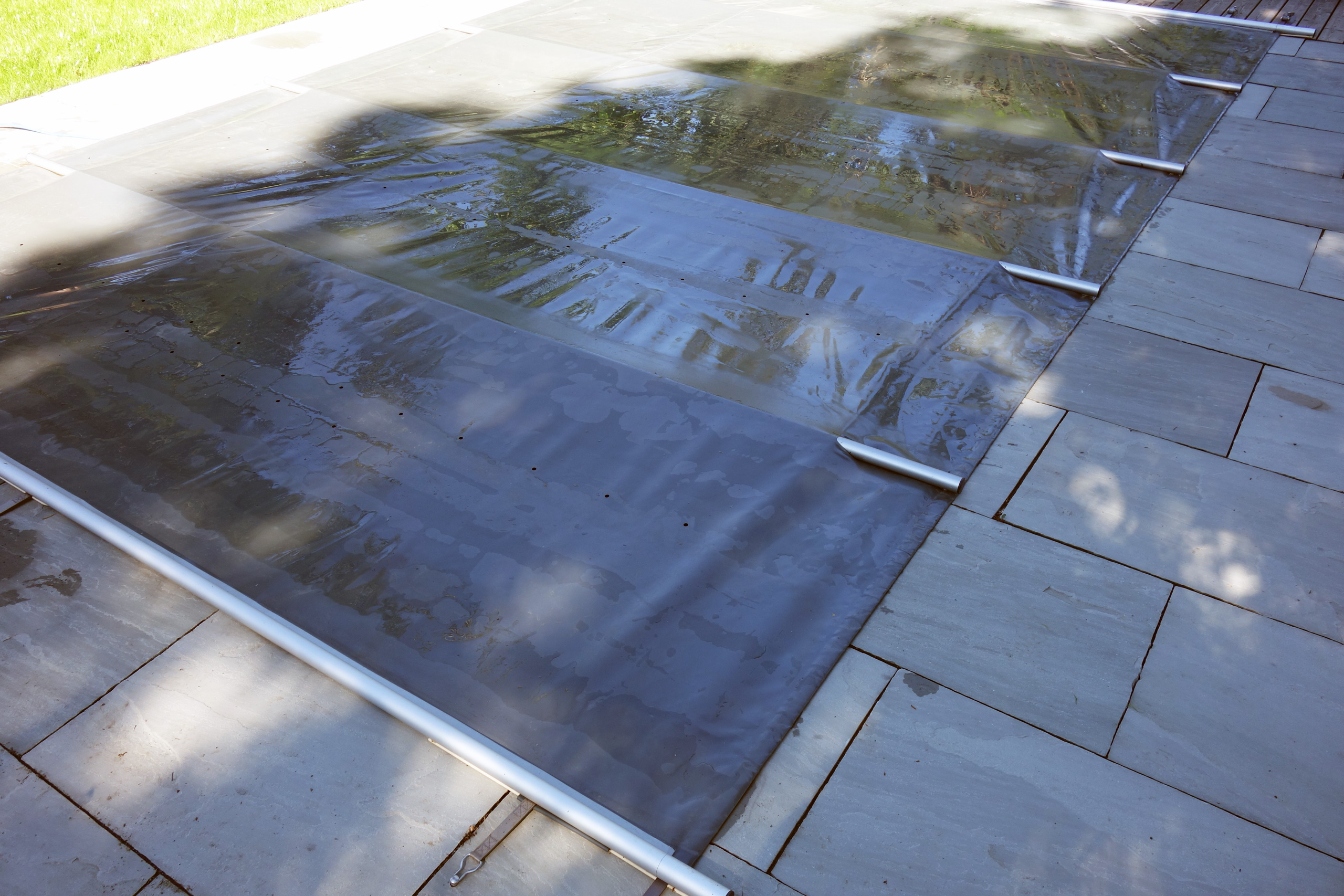 Abdeckung eines Rechteck-Pools mit gerader Treppe, die Poolfolie ist mit Stangen gesichert.