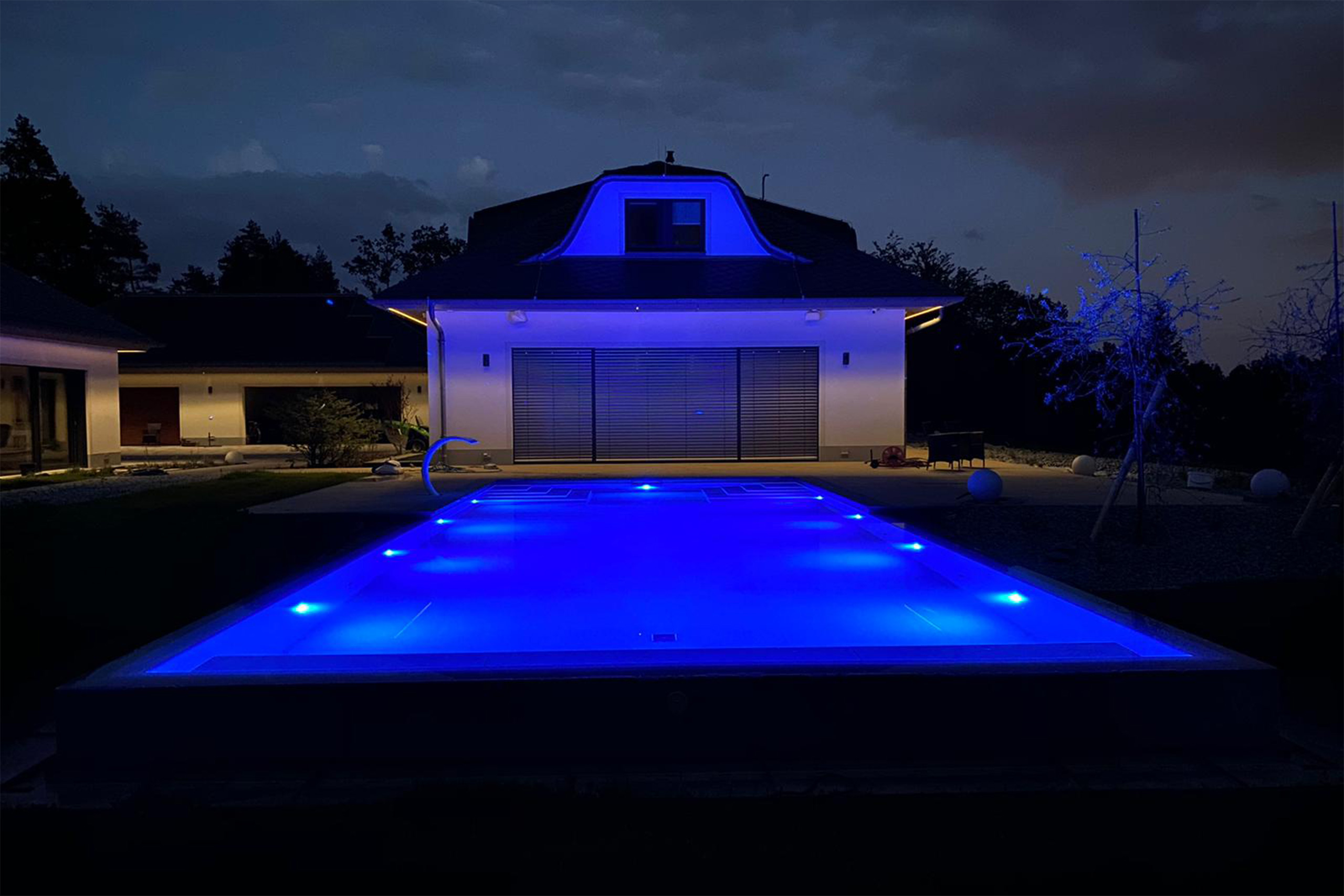 Überlaufbecken bei Nacht mit blauer Unterwasserbeleuchtung vor dem Haus