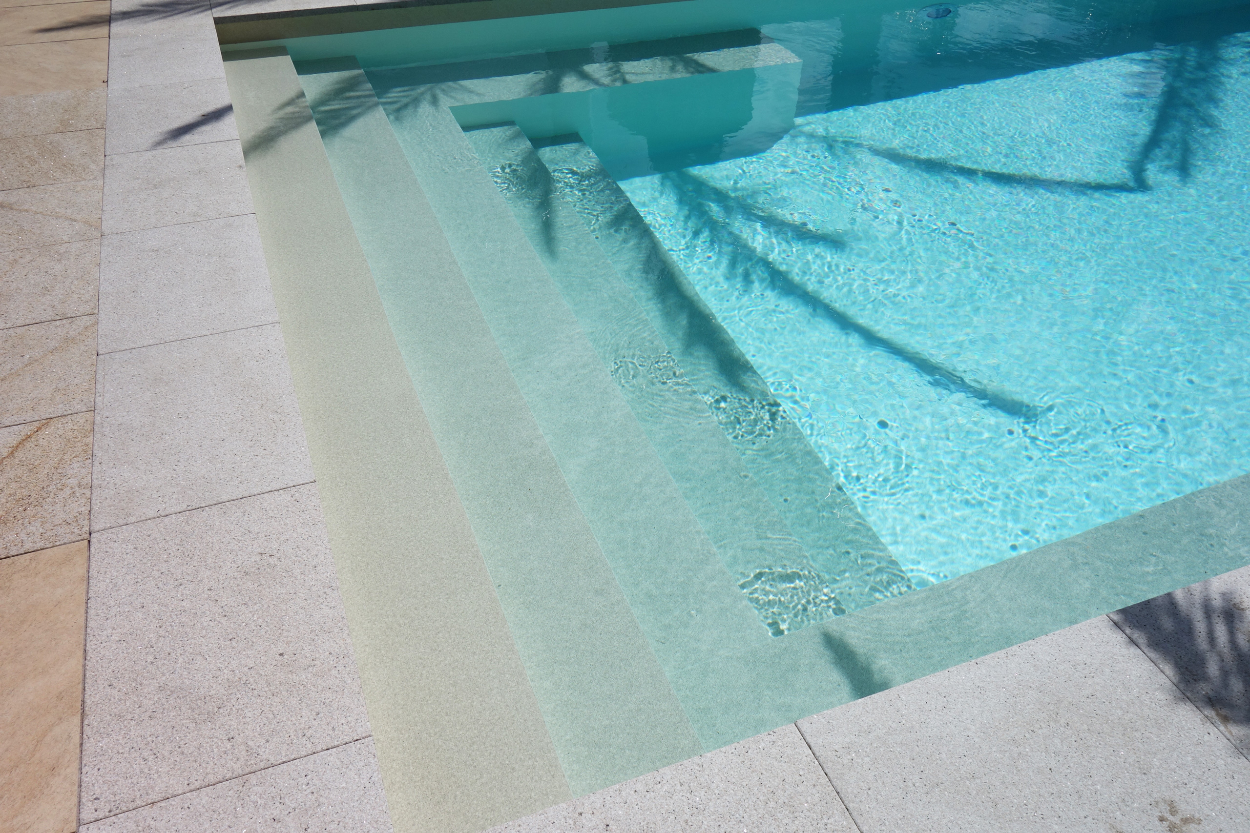 Gerade Treppe und Podest des Schwimmbades, umgeben von hellen Poolrandplatten