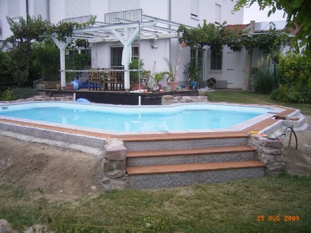 L-förmiges Schwimmbecken mit trapezförmiger Treppe und Holzstufen im Garten