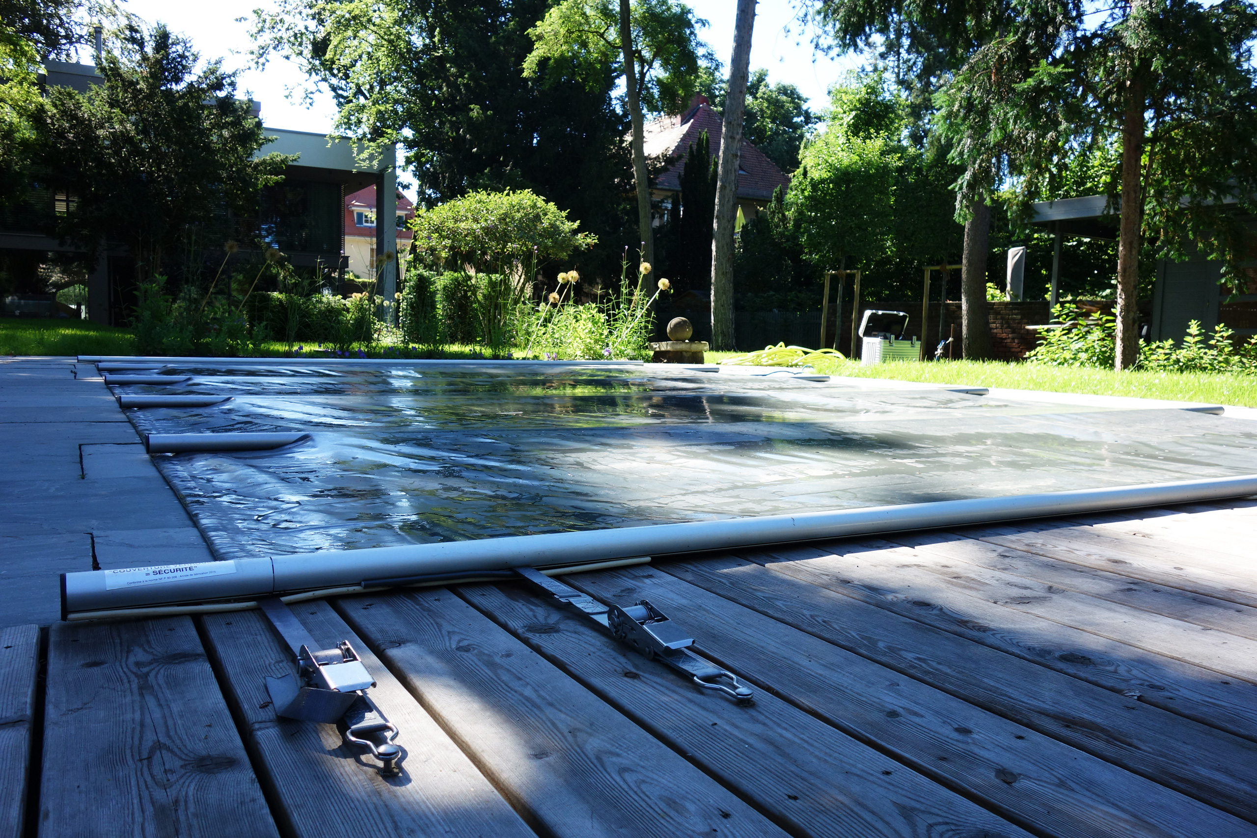 Abgedeckter Pool mit Sicherheitsabdeckung und Spanngurten auf Holzterrasse