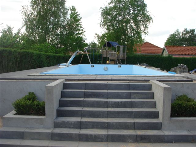 Treppe aus dunklen Steinplatten führt zu einem blauen Pool mit Schwalldusche und GSA, umgeben von Hecken.