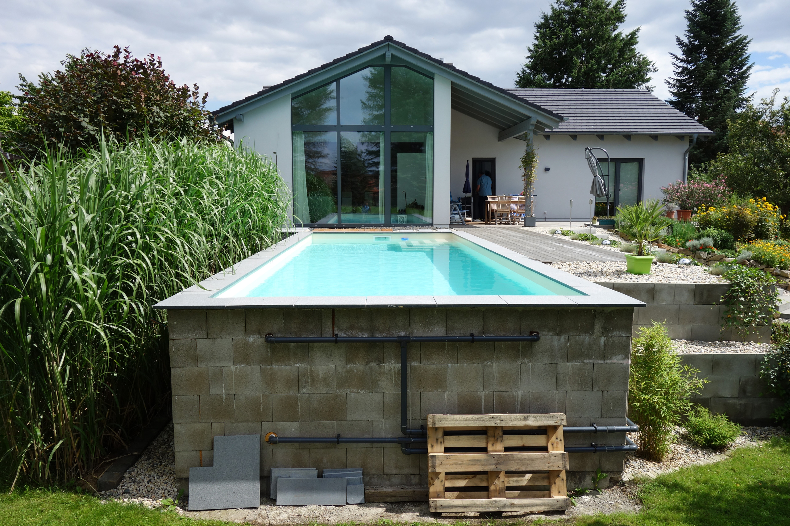 Rückseite eines herausstehenden Swimmingpools mit sichtbaren Rohrleitungen und Betonsteinen
