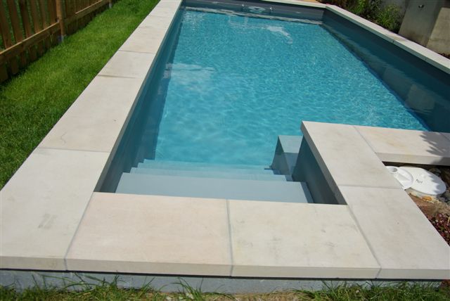 Eingelassenes Schwimmbecken mit grauer Treppe und hellen Beckenrandsteinen, umgeben von Rasen