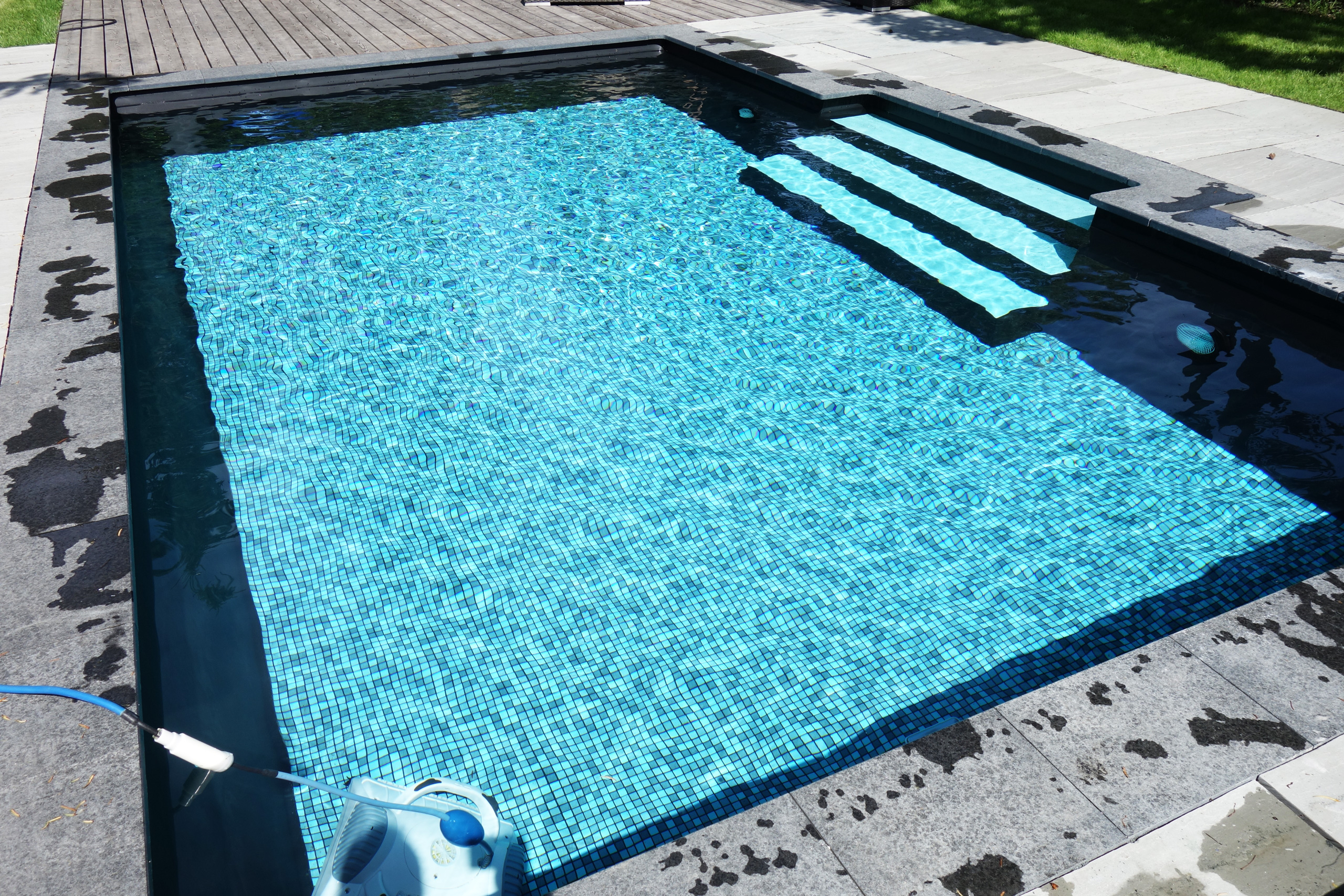 Blick von oben auf einen rechteckigen Pool mit blauer Mosaikfolie und gerader Treppe