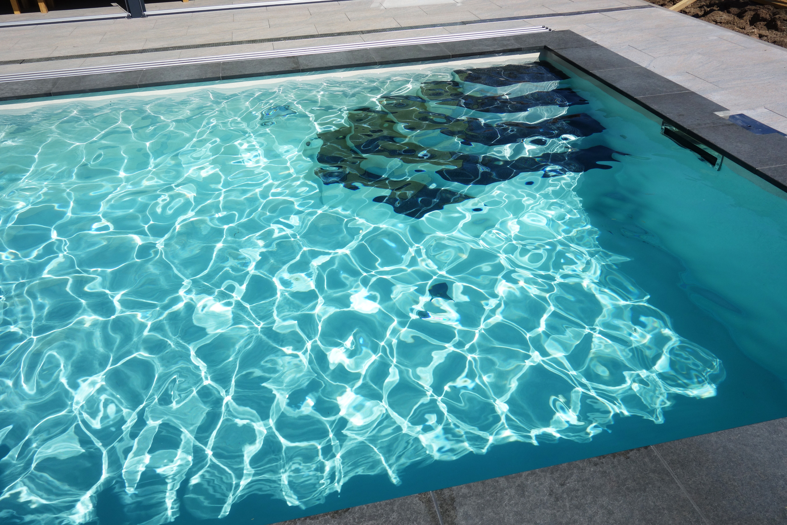 Blick von oben auf die Treppe eines Rechteck-Schwimmbades mit türkisblauem Wasser und Gegenstromanlage