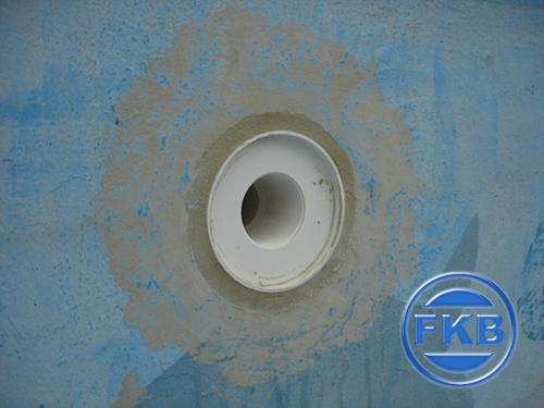 Detailaufnahme eines weißen Rohrs in einer hellblauen Beckenwand, umgeben von Mörtel