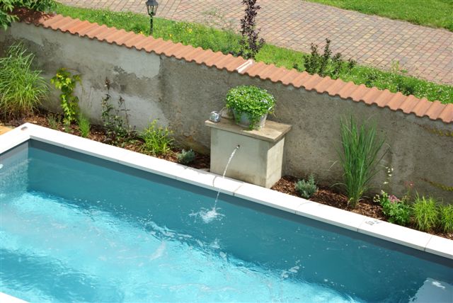Teilansicht des Schwimmbeckens mit Wasserspeier, umgeben von einer Bepflanzung mit Gräsern und Sträuchern