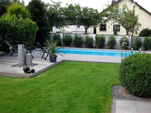 Langes, rechteckiges Schwimmbecken mit türkisem Wasser im Garten, umgeben von Holzterrasse und Rasen