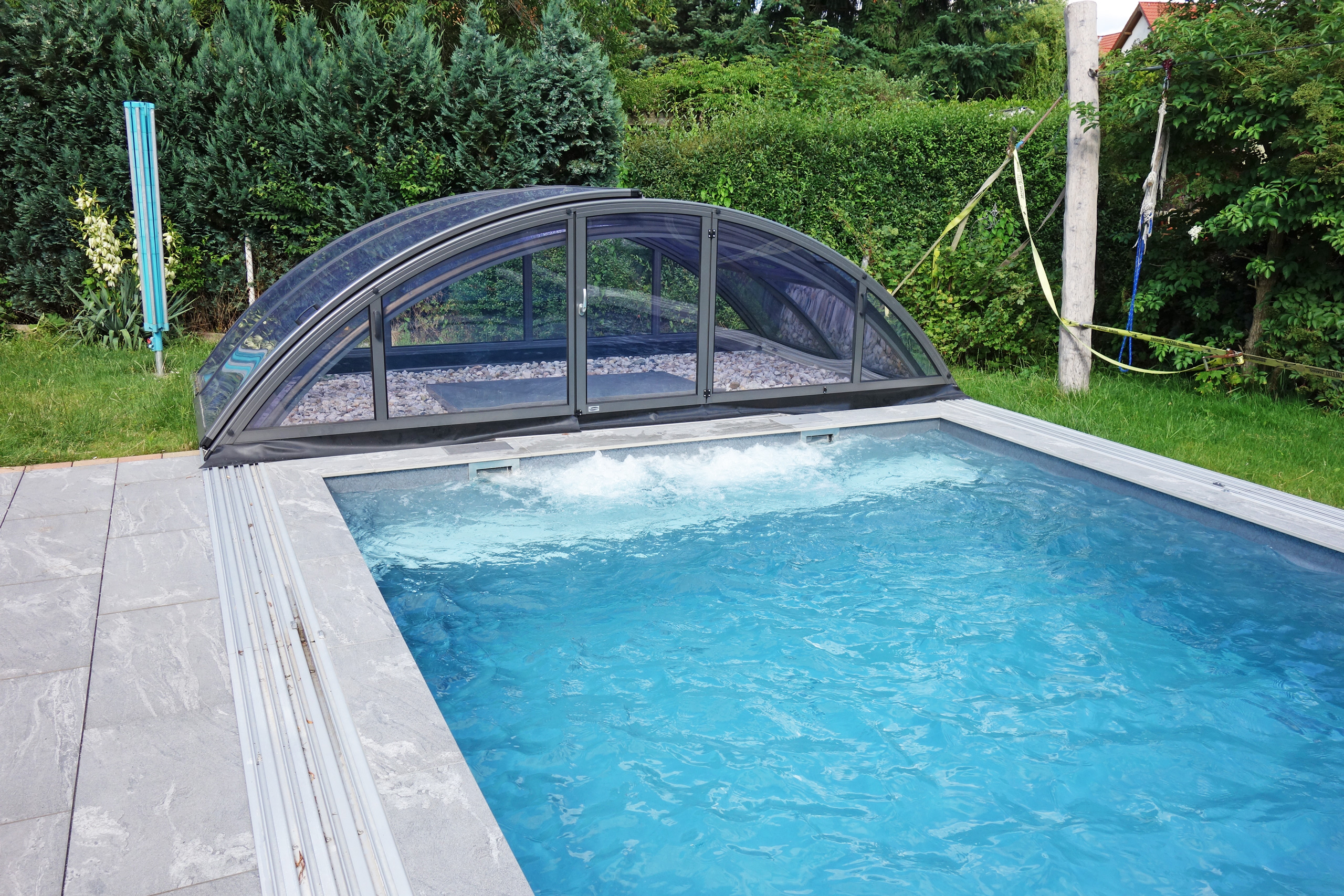 Schwimmbecken mit Überdachung, Ecktreppe und Podest, umgeben von Garten und Terrasse