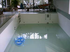 Hallenbad mit weißer Folie, Treppe und Einbauteilen, Wasseroberfläche spiegelt Deckenfenster wider